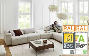 Großzügiges, helles Wohnzimmer mit bodentiefen Fenstern und modernem, beigem Ecksofa. Ein Paar sitzt entspannt auf dem Sofa und genießt gemeinsam ein Buch.